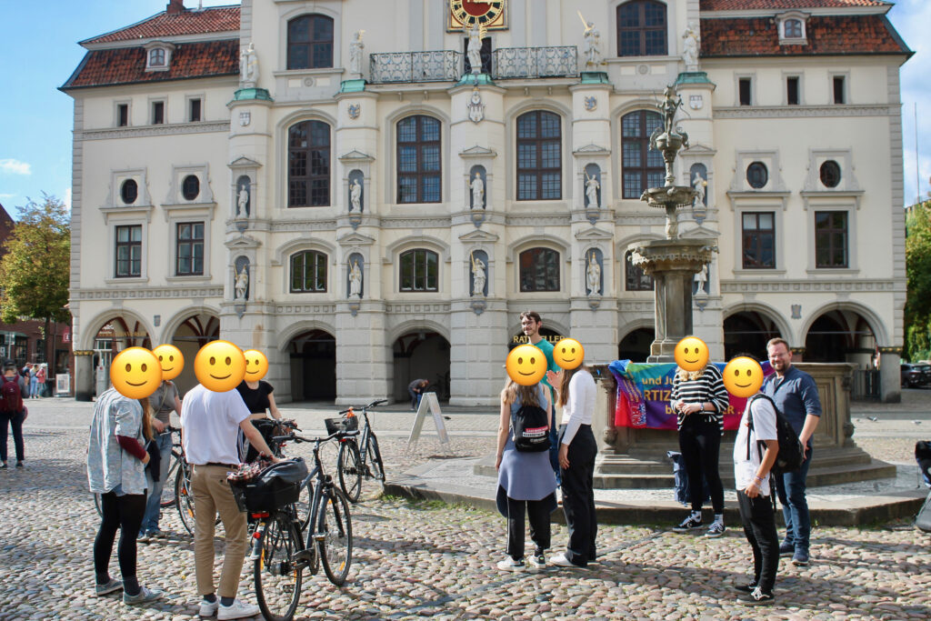 Eine Gruppe junger Menschen auf dem Lüneburger Marktplatz vor dem Luna-Brunnen und dem historischen Rathaus Lüneburg.