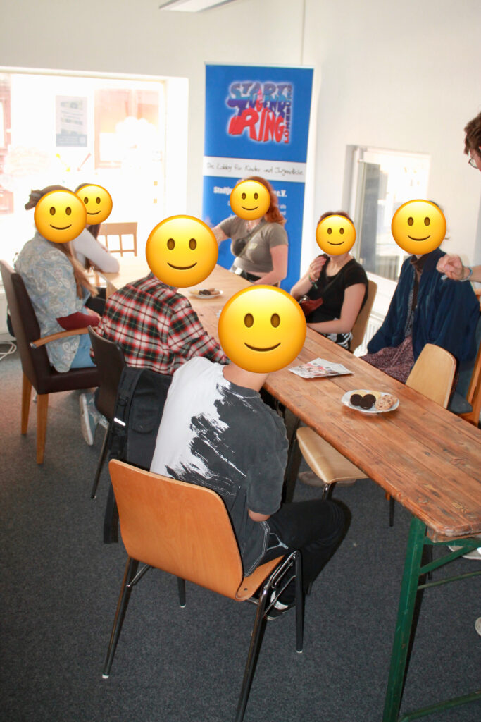 Eine Gruppe Jugendlicher um einen Tisch, bei lecker Keksen, tauschen sich zu den Räumen und deren Möglichkeiten der Nutzung aus.